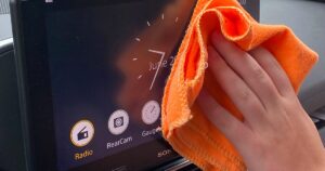 A person's hand wiping a car audio touchscreen with an orange cloth