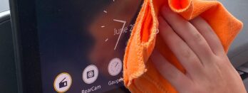 A person's hand wiping a car audio touchscreen with an orange cloth